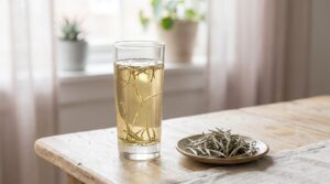 Bourgeons de thé blanc argentés infusant dans un verre transparent, à côté d'une coupelle de bourgeons secs