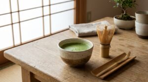 Bol à matcha en céramique rempli de thé matcha mousseux, avec son fouet et sa cuillère en bambou sur une table en bois clair
