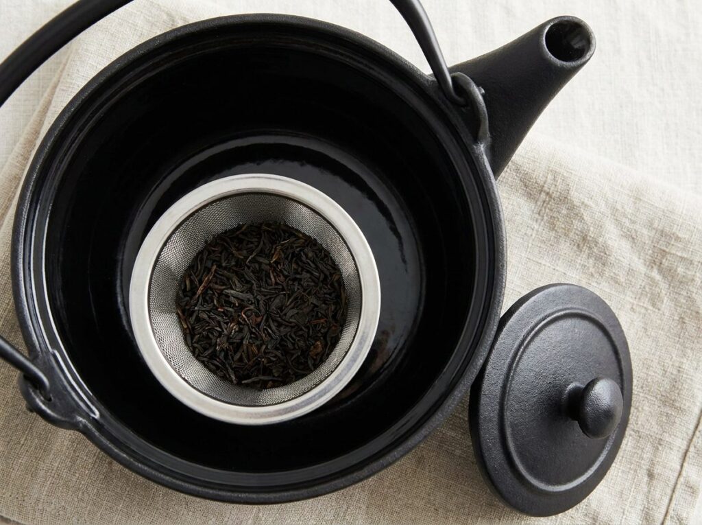 Intérieur émaillé noir d'une théière en fonte avec son filtre en inox rempli de feuilles de thé
