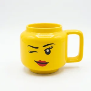 39c1a5dd-0be8-4419-a2b9-9ec71a82a12a.webp Mug jaune en forme de tête de personnage avec un visage qui fait un clin d'œil