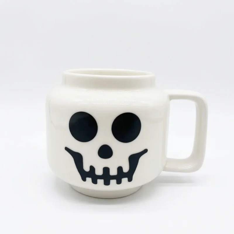 509637c4-87f4-4322-b59d-f799e2b354e2.webp Mug en céramique blanche représentant un crâne souriant avec une anse rectangulaire classique